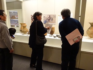 当センター職員が展示室の県町遺跡出土品の前で解説をしている様子。