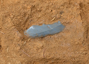 下半分が土に埋まった状態の灰色の石器が1点写っています。長方形に近い形をしています。