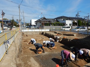 7人ほどの作業員が、両刃鎌や移植ごてを使って土を掘っている様子。